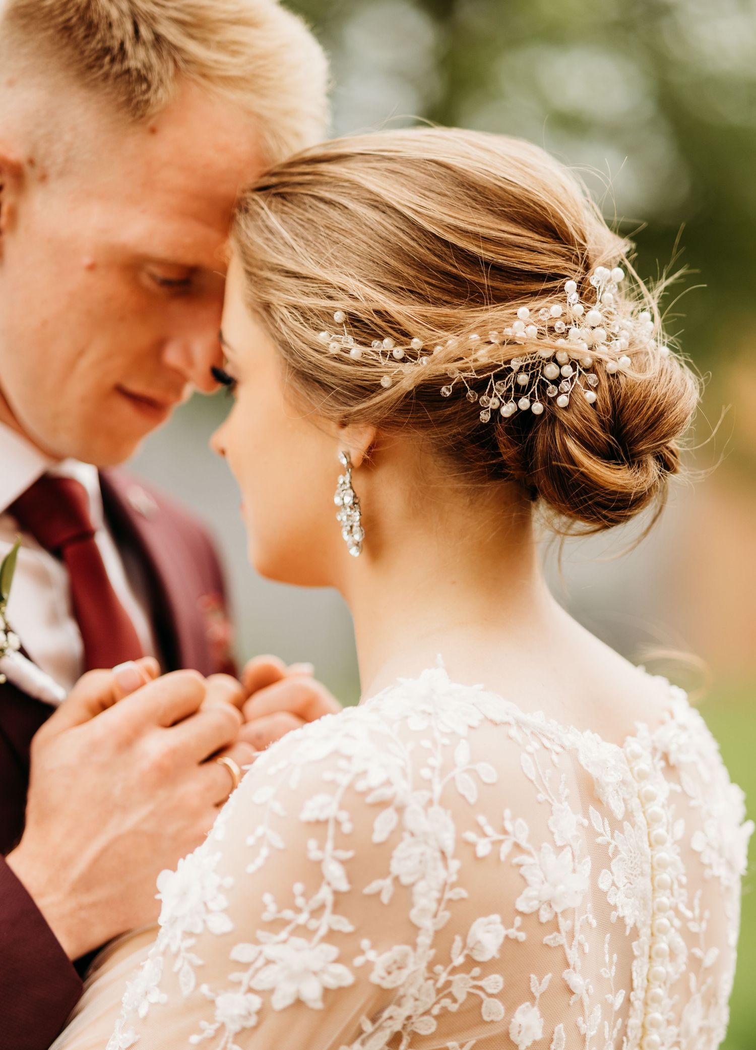 Close-up of elegant bridal hairstyle with crystal hairpiece and lace dress details.