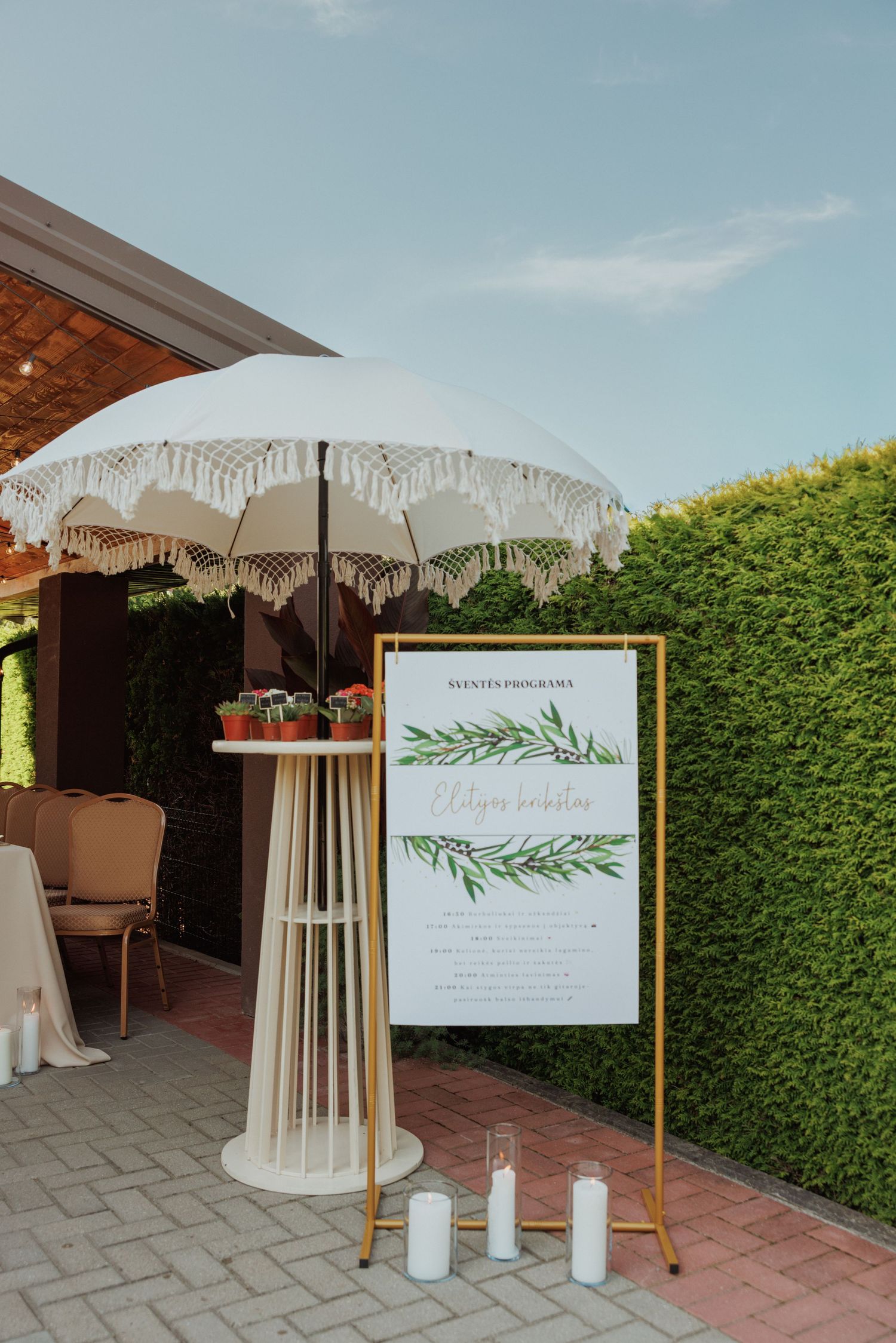 Outdoor event setup with white umbrellas and greenery-themed welcome signs.