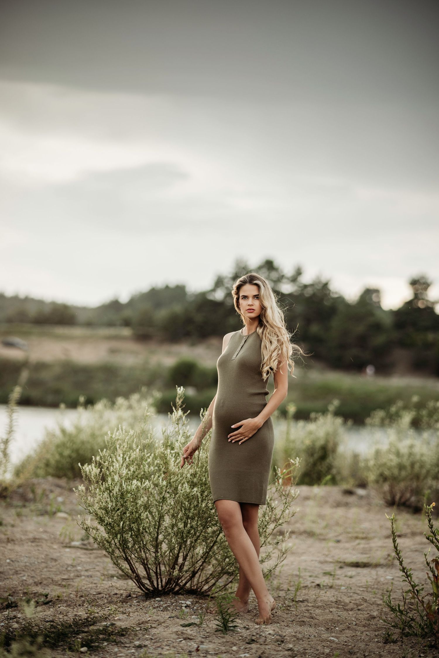 Artistic maternity photos taken near water with desert brush and moody lighting.