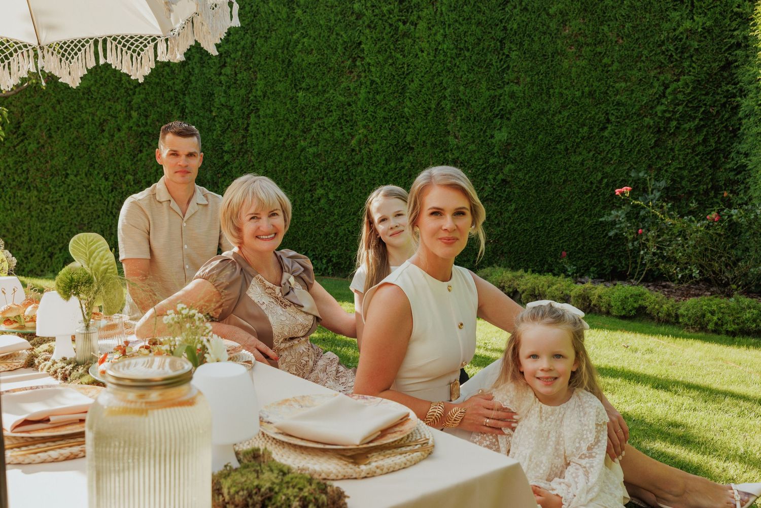 Outdoor garden party setting with elegant table decorations and hedges in background.