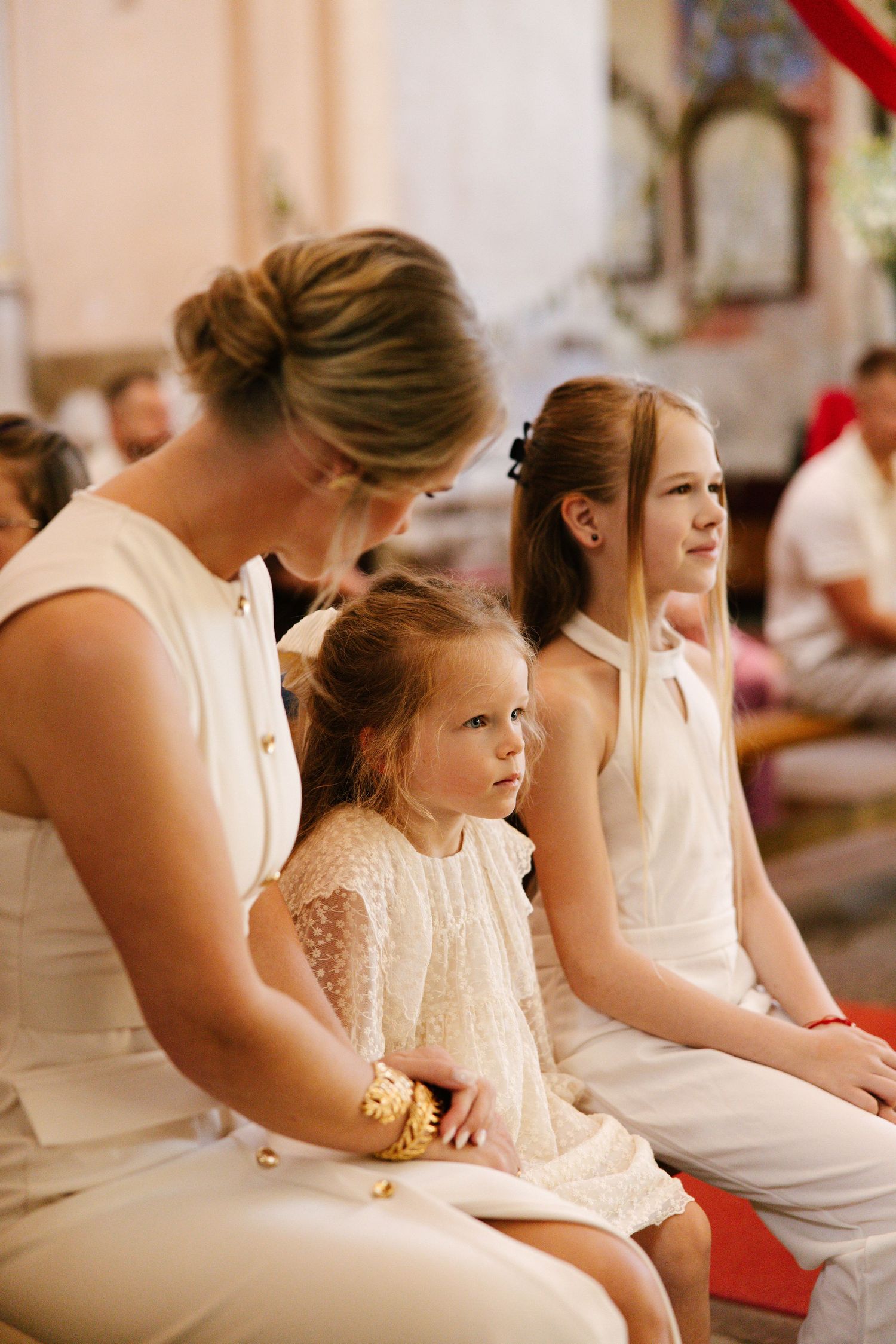 Several people in white dresses sit together during a formal church ceremony.