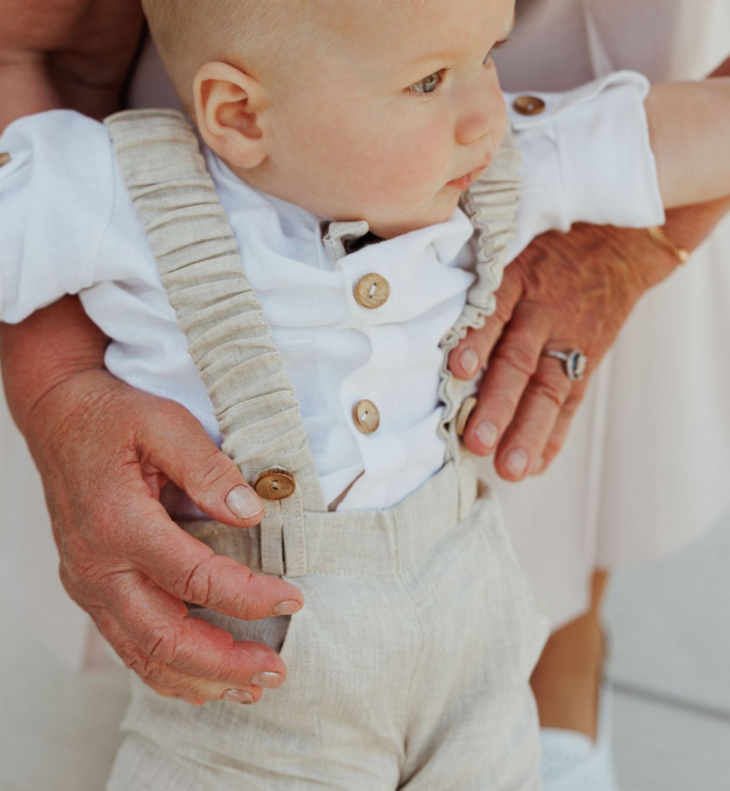 Close-up details of beige overalls with decorative buttons and white clothing.