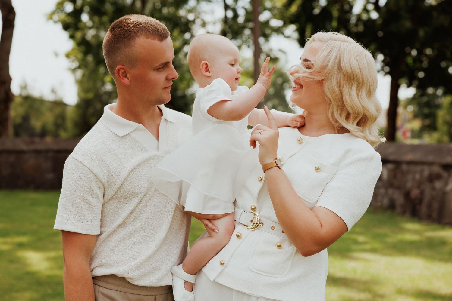 Family in white clothing sits together on grass during a sunny outdoor photo session.