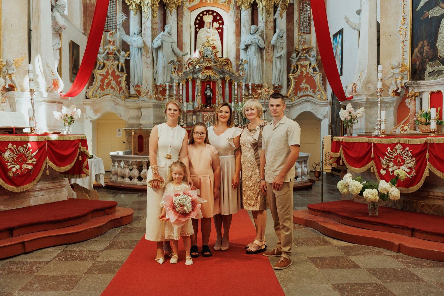A group stands together in a beautifully decorated Catholic church with ornate altar and red drapery.