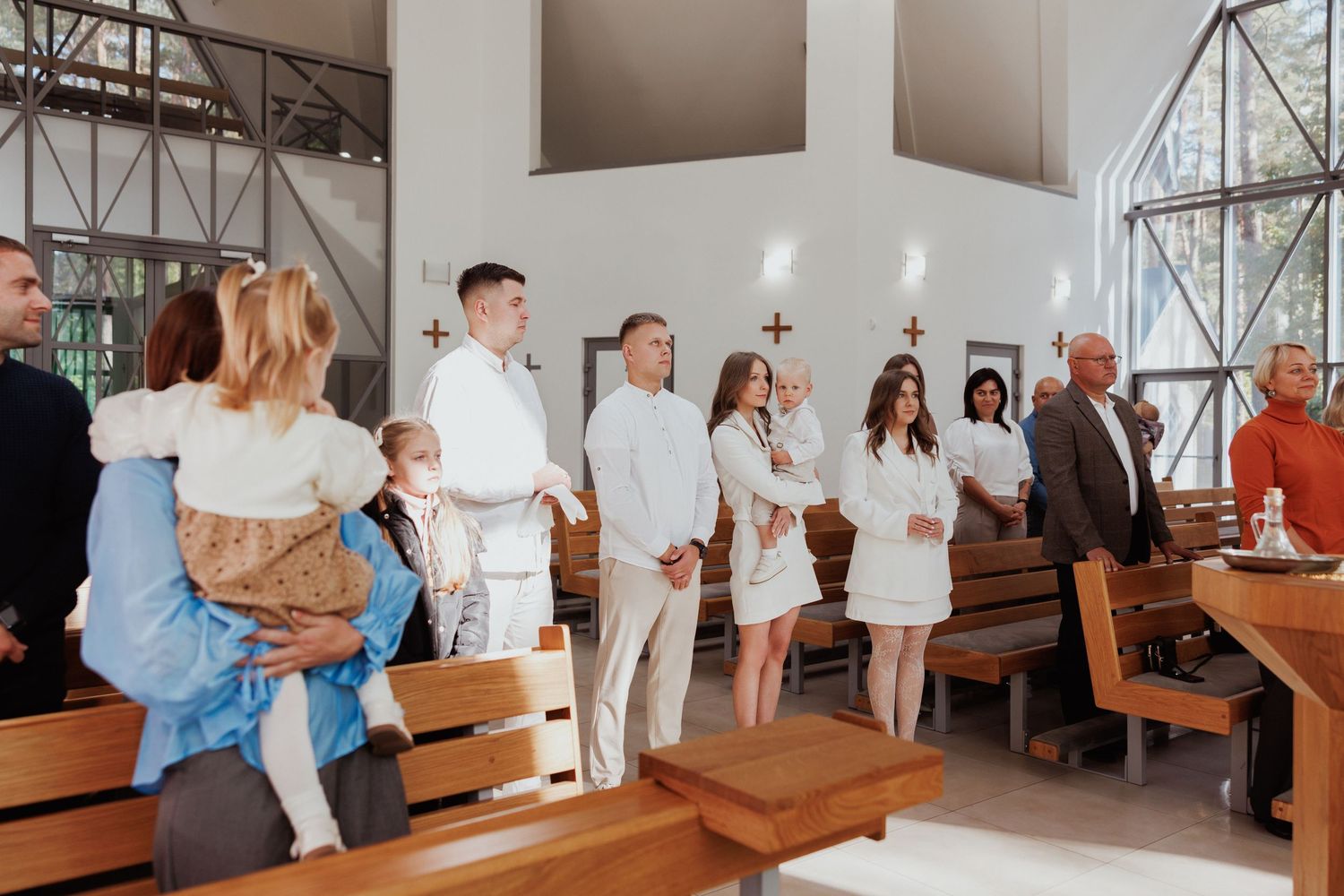 A panoramic view of a church ceremony with people standing in white clothing along wooden pews.