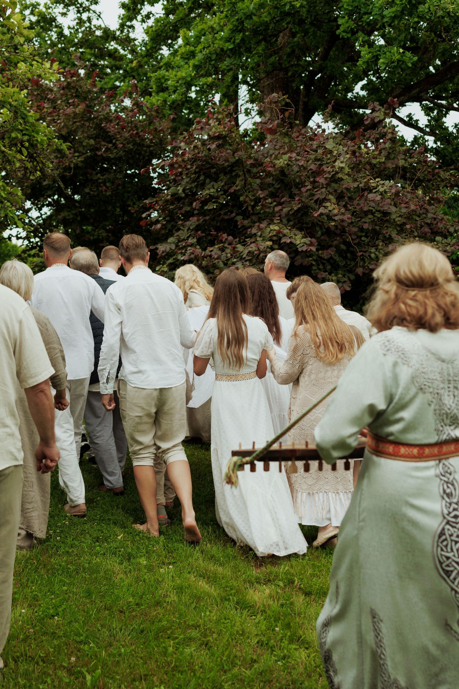 Group of people in traditional white attire walking barefoot on grass during an outdoor ritual.