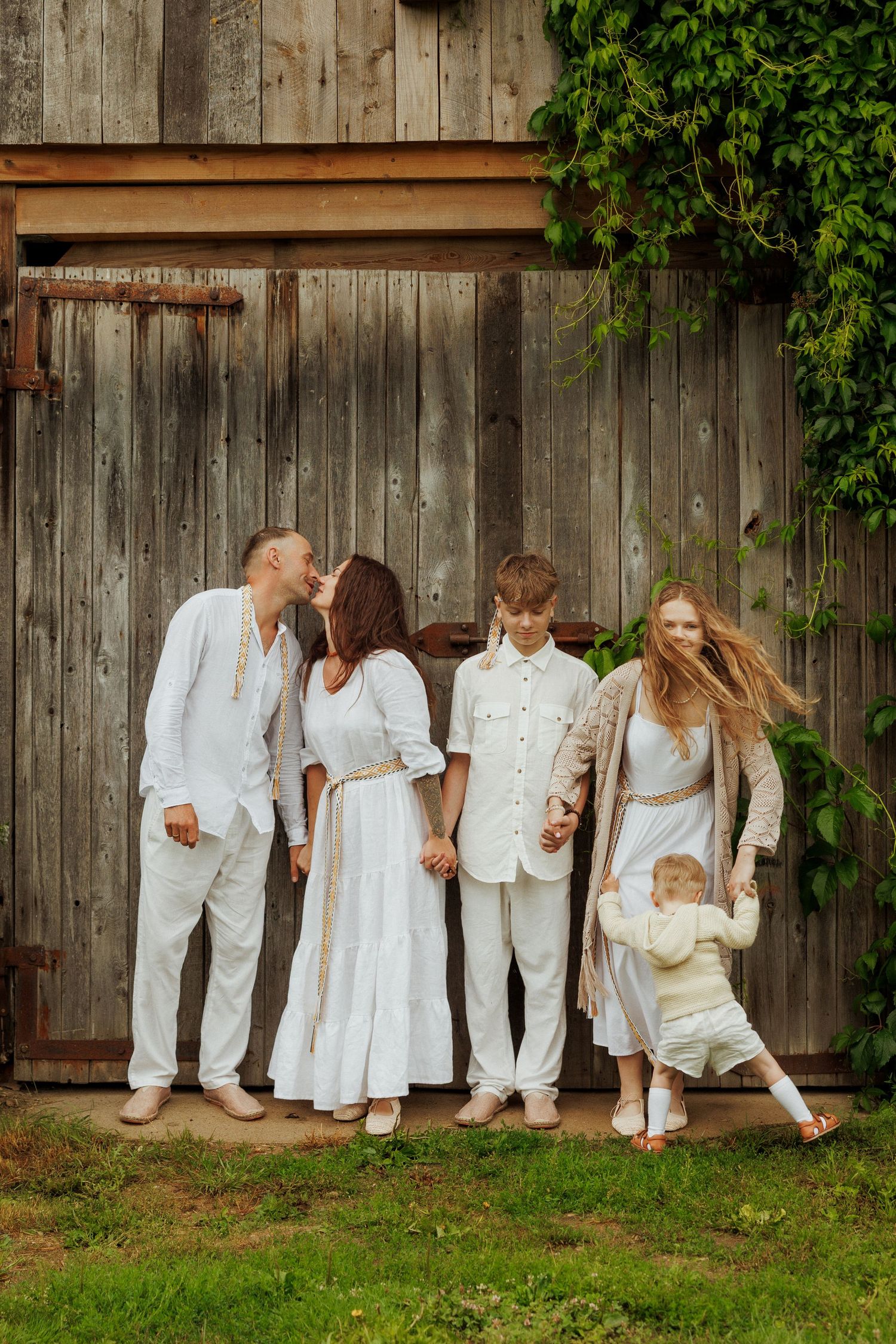 Family of five in matching white outfits posing together in front of a rustic wooden barn door outdoors.