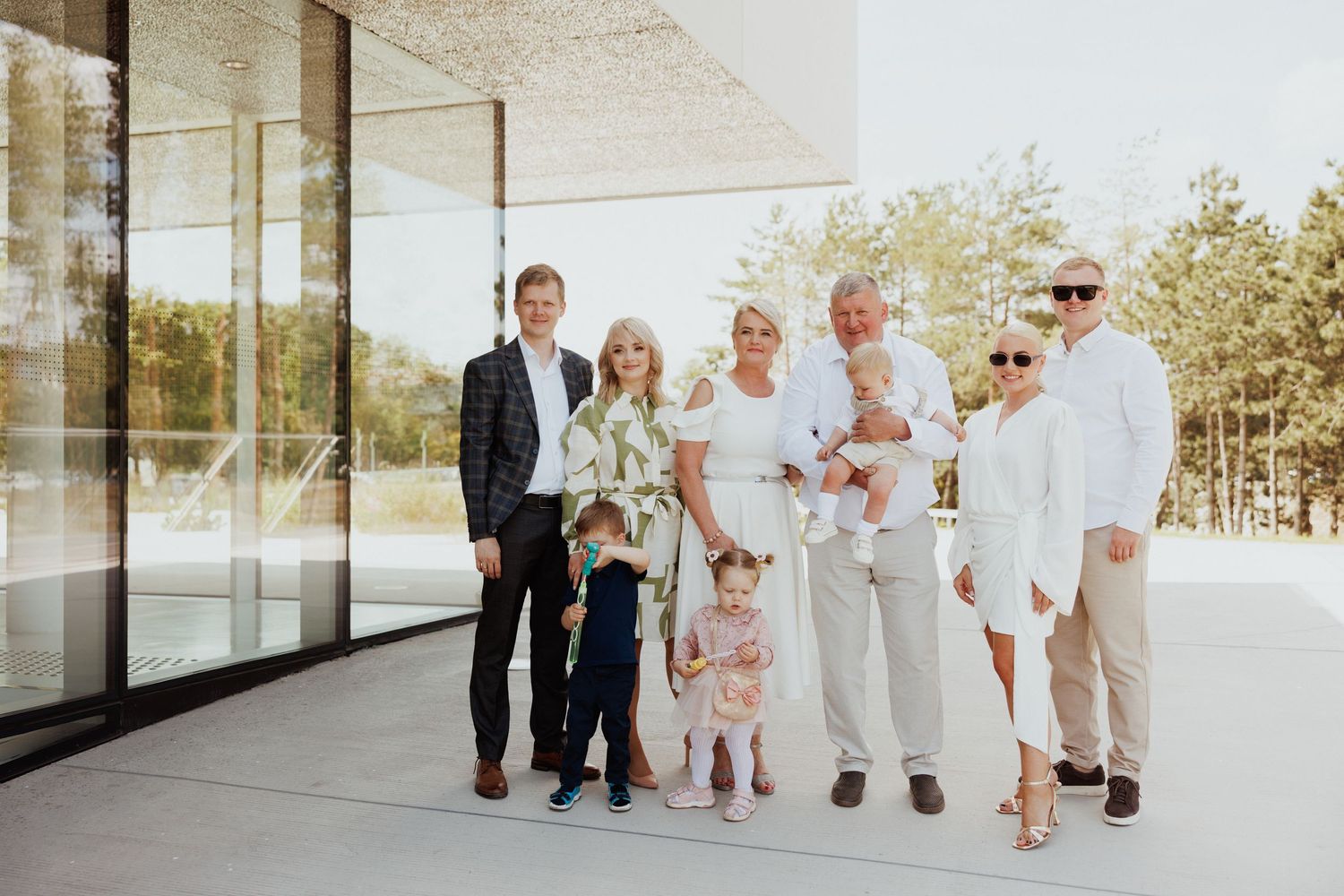Wedding party in light colored attire poses together outside a modern building.