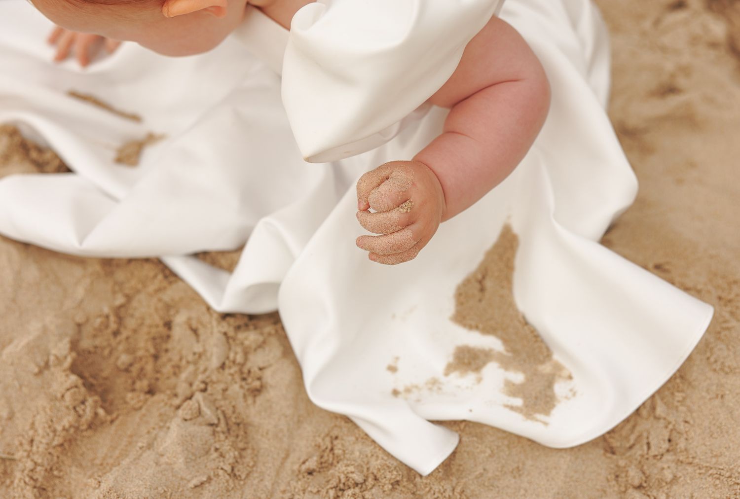 A person's hands crumple up white paper tissue into balls on a beige textured surface.