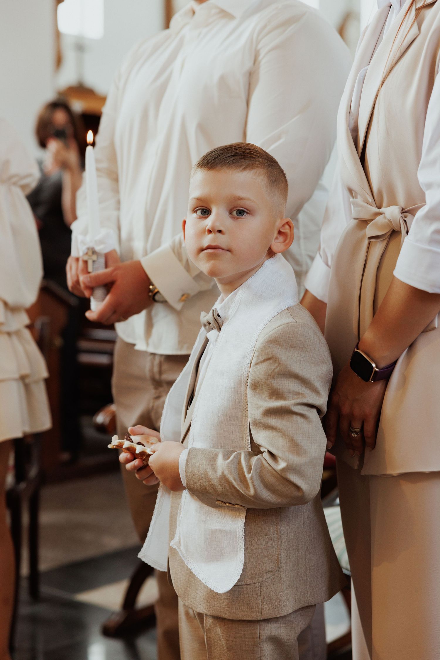 A young attendee in a light beige suit stands attentively during a formal indoor event.