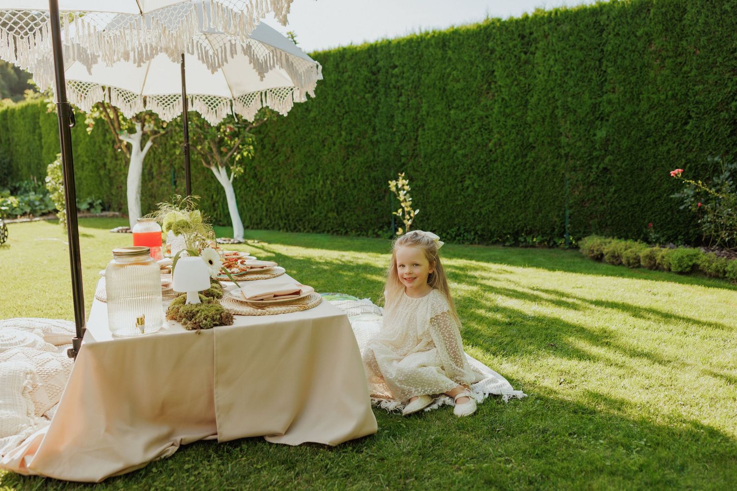 A wedding celebration in a lush garden setting with tall hedges and elegant white decor elements in natural sunlight.