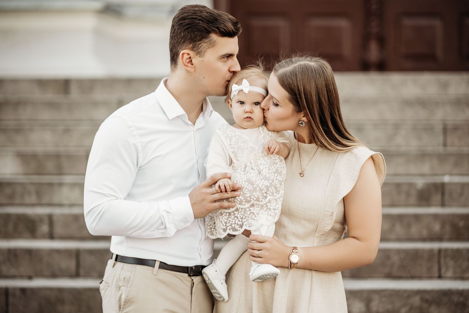 Family sitting together on stone steps outdoors in coordinated white and neutral outfits.
