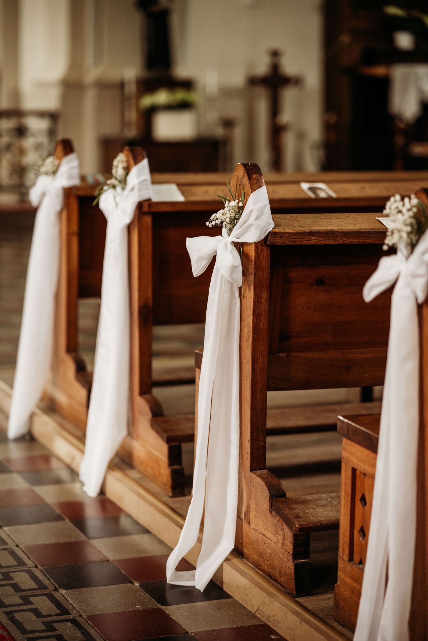 Church pews decorated with elegant white bows and fabric for a wedding ceremony.