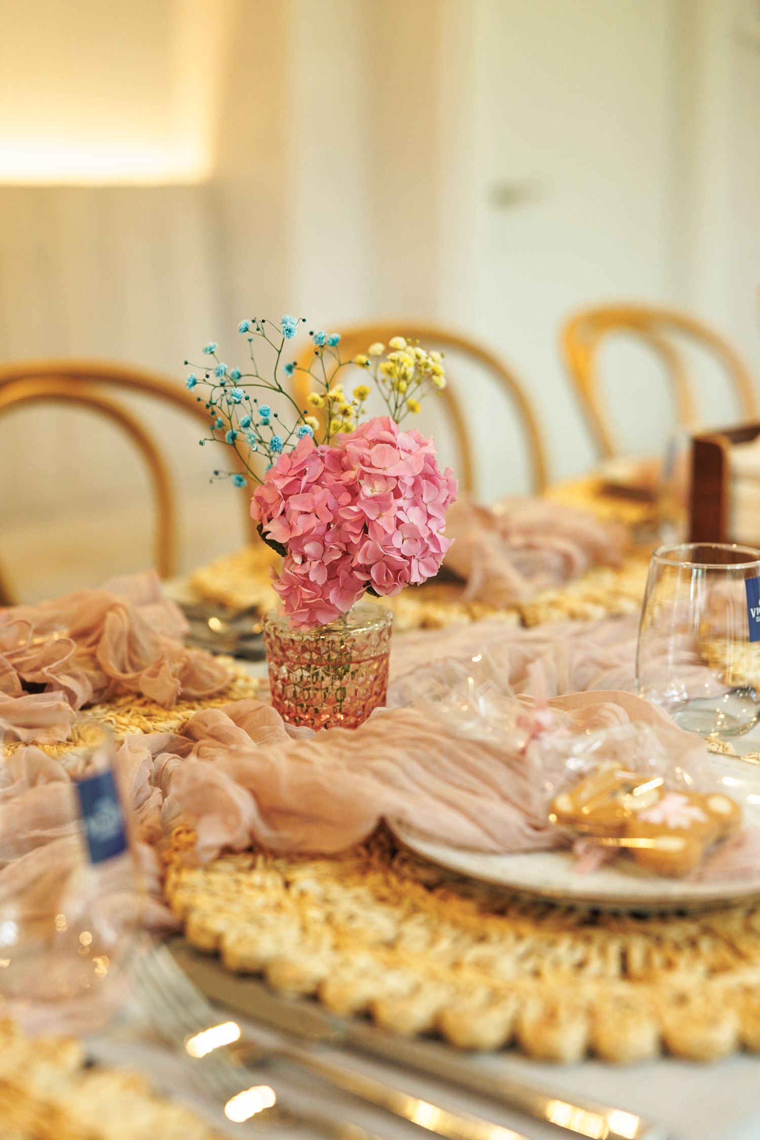 Elegant table setting with pink floral centerpiece and golden accents for a special celebration.