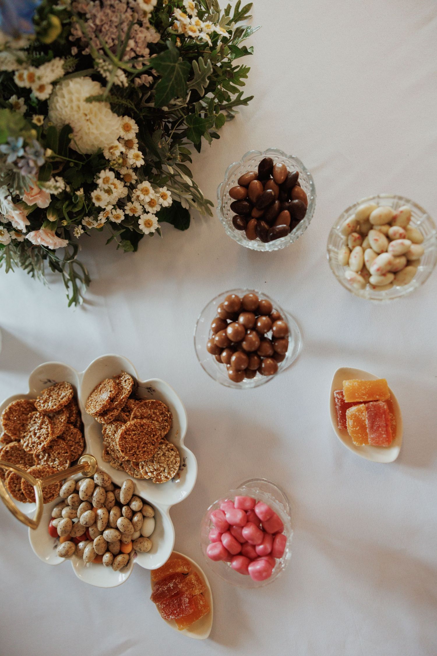 Assorted nuts, dried fruits, and pastries arranged on white serving plates with floral decorations.
