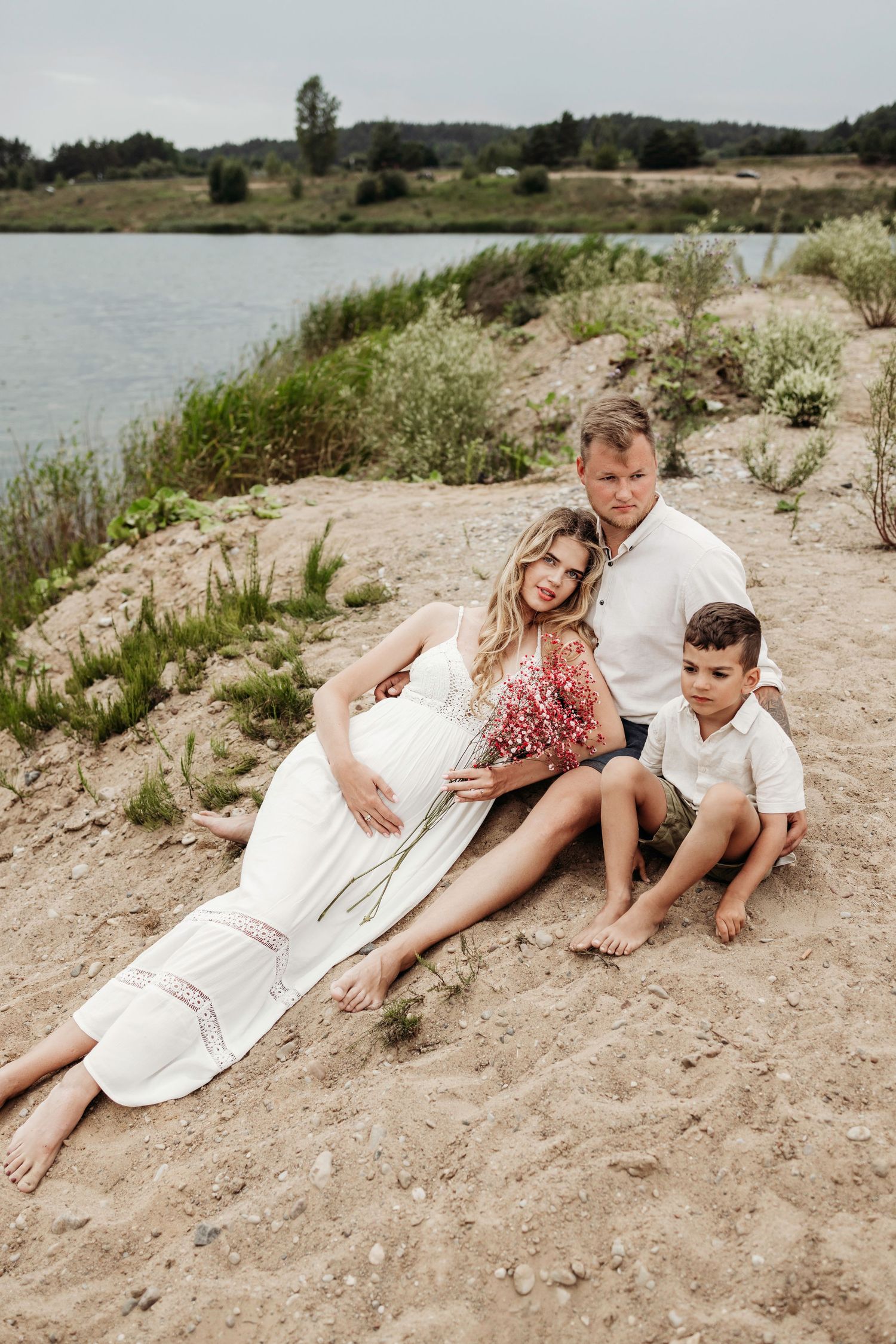 Family relaxing together on a sandy beach slope near water.