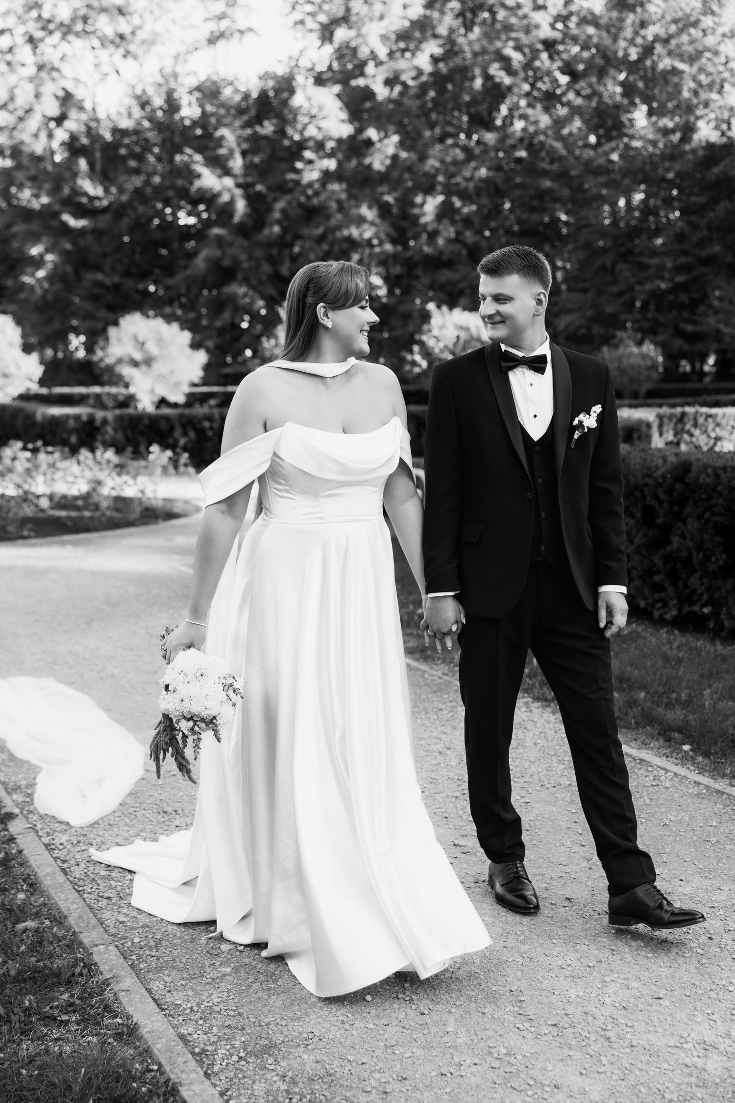 Black and white series showing flowing white wedding dress train on a garden path.
