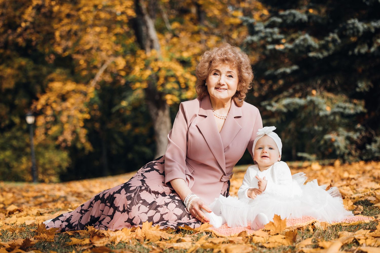 Two people sit together on fallen autumn leaves in a park during golden hour.