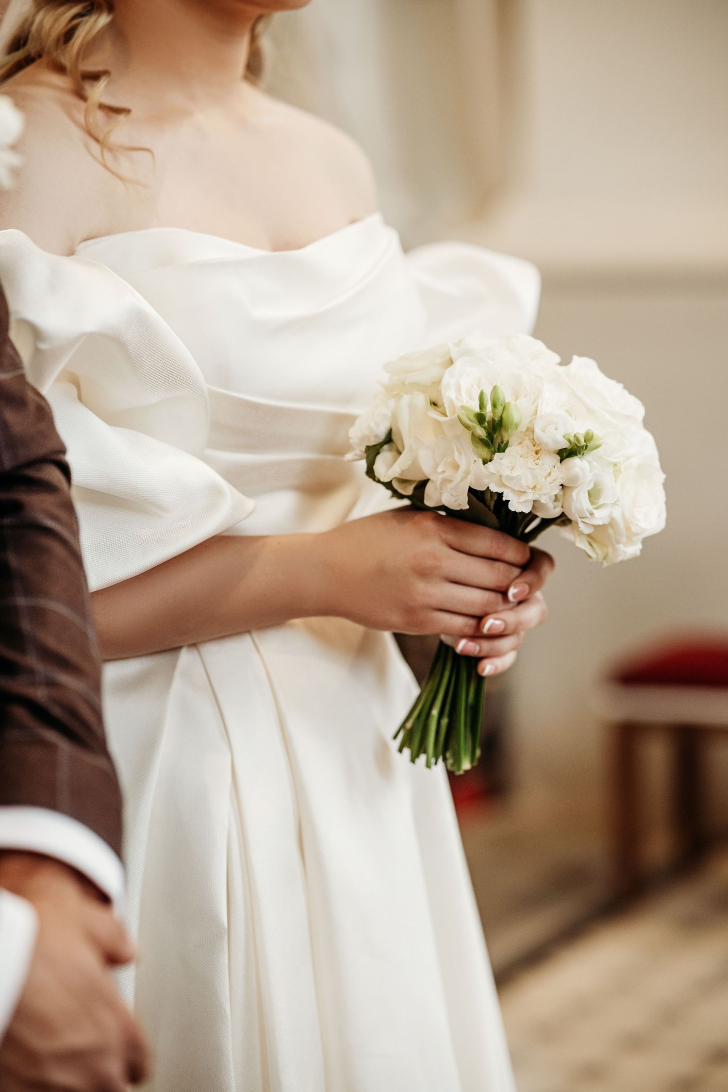 Close-up detail of a white wedding dress with a delicate bouquet of white flowers held against the fabric.