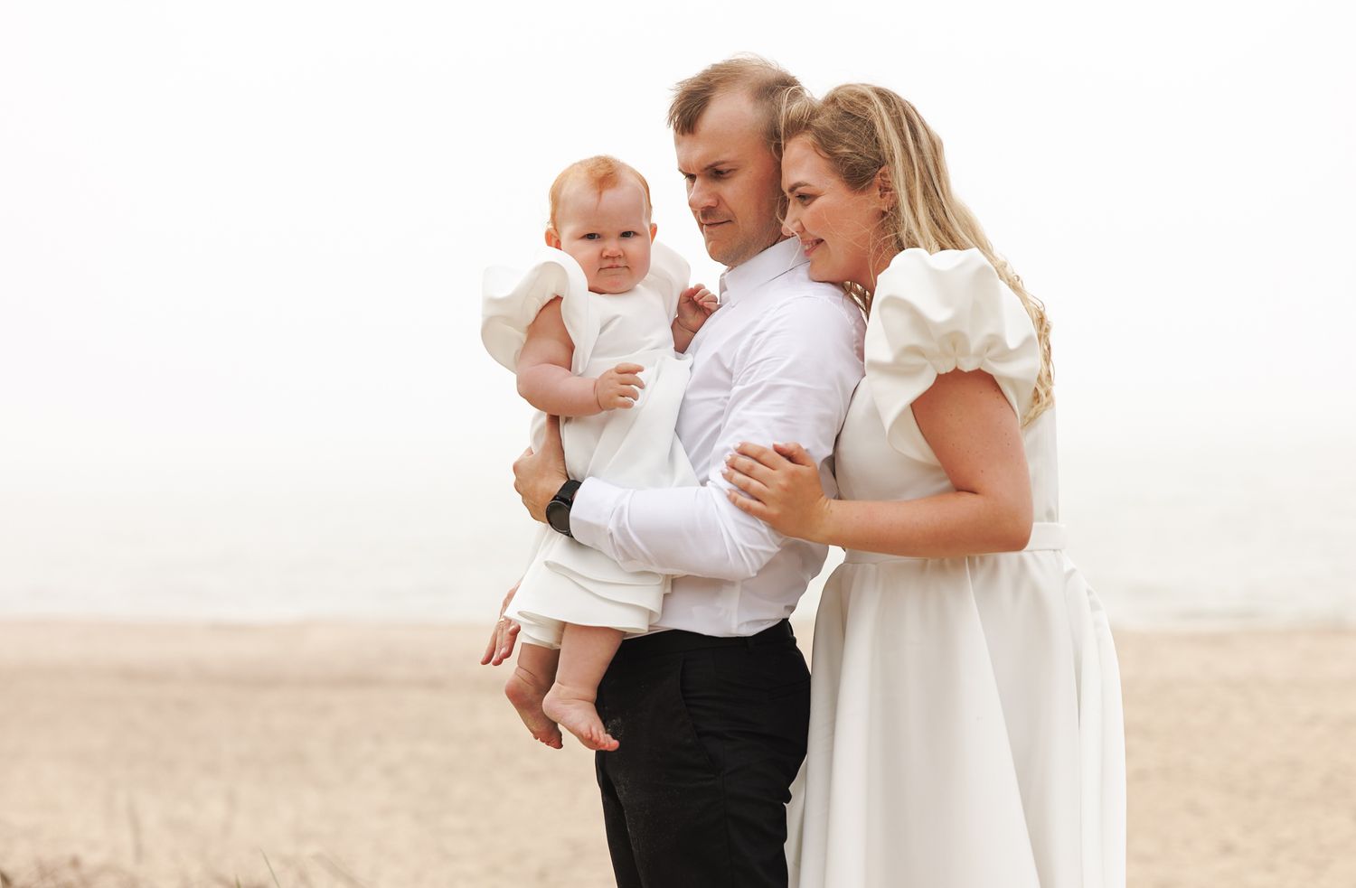 Family wearing white and black outfits poses together on a beach during sunset for portraits.