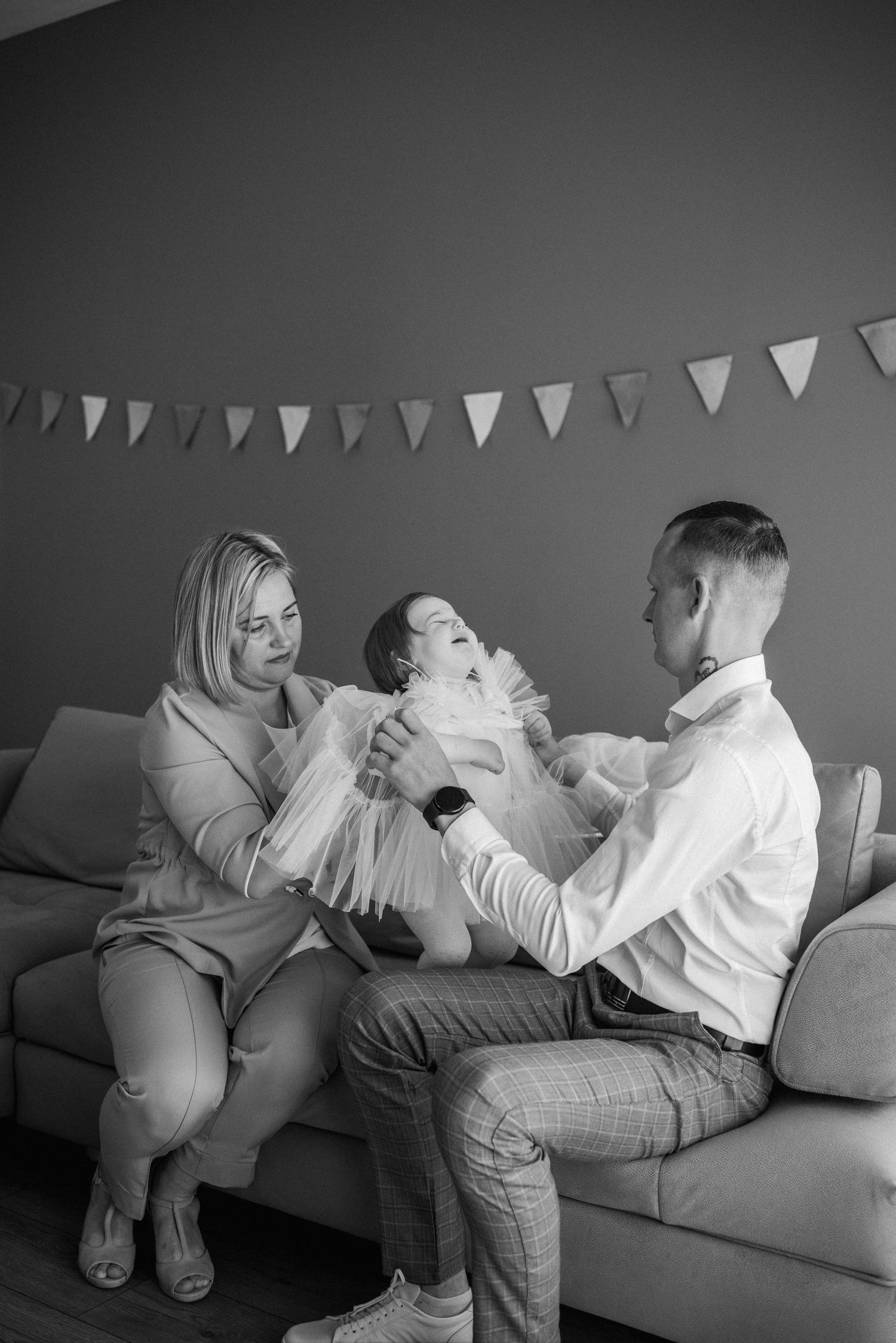 A black and white photo of a family sitting on a couch under party bunting, sharing a tender moment together.