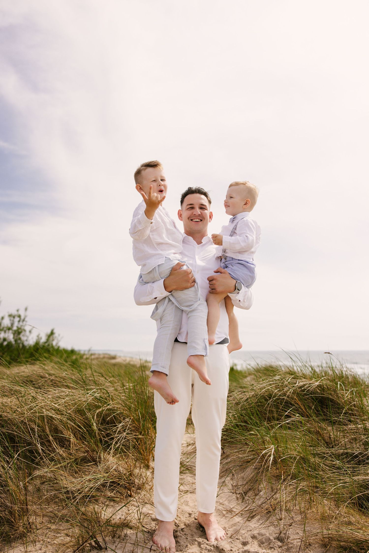 Family photoshoot on sandy dunes wearing all white clothing against cloudy sky.