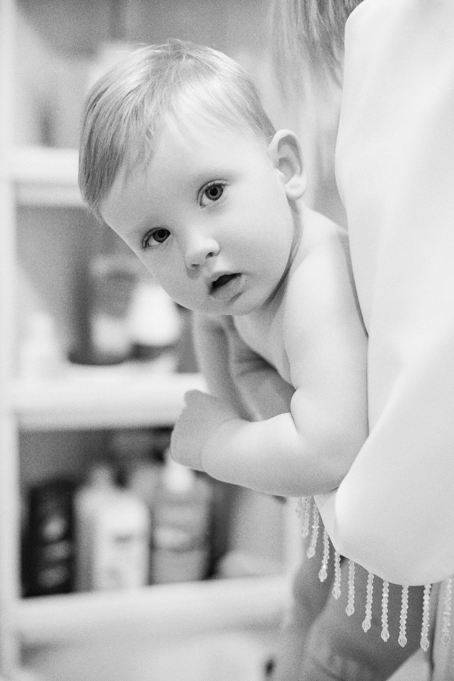 A black and white portrait of a curious baby peering over a surface with soft lighting and shallow depth of field.