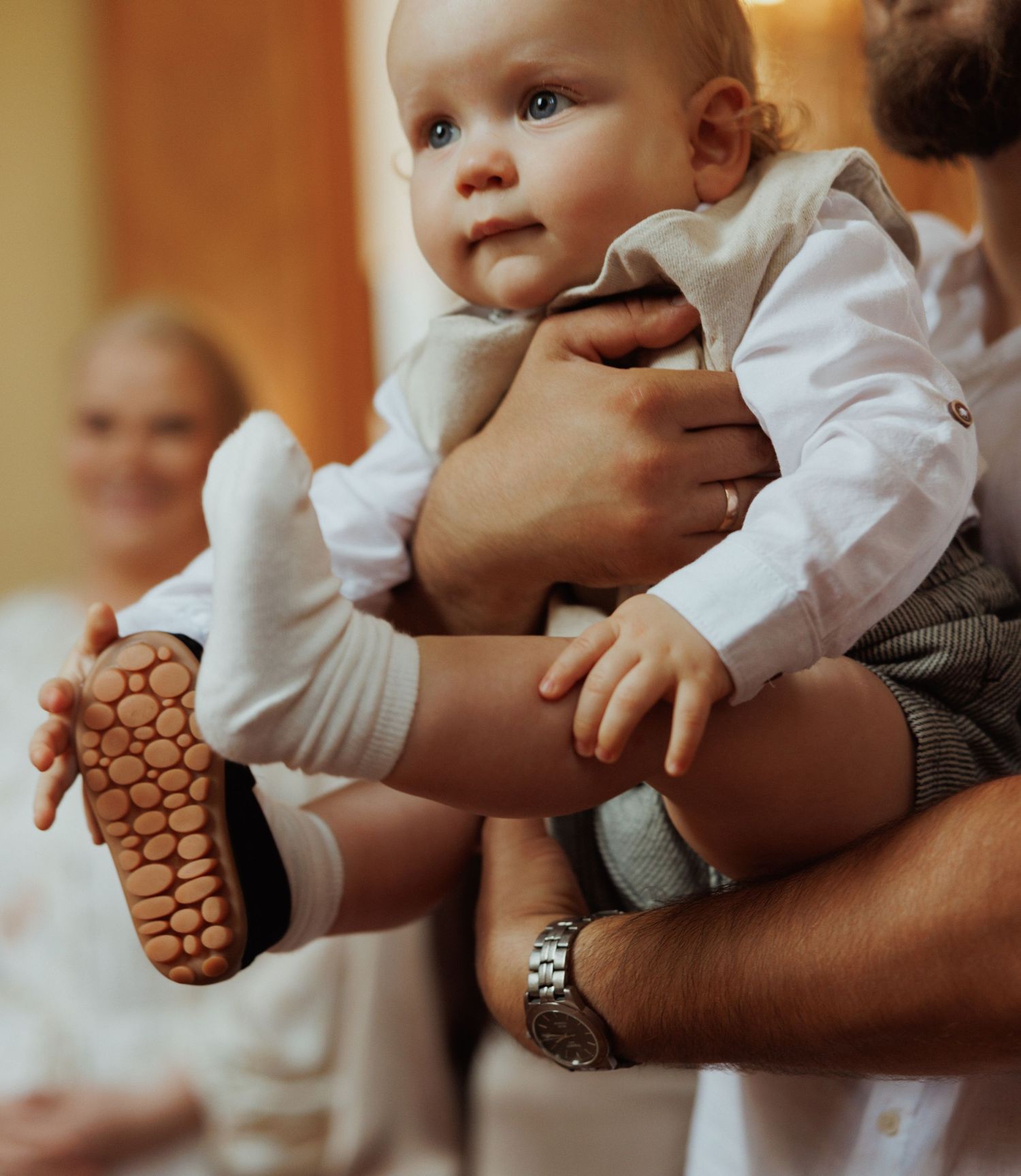 Baby wearing white shirt and socks being held while showing grippy non-slip soles on their feet.