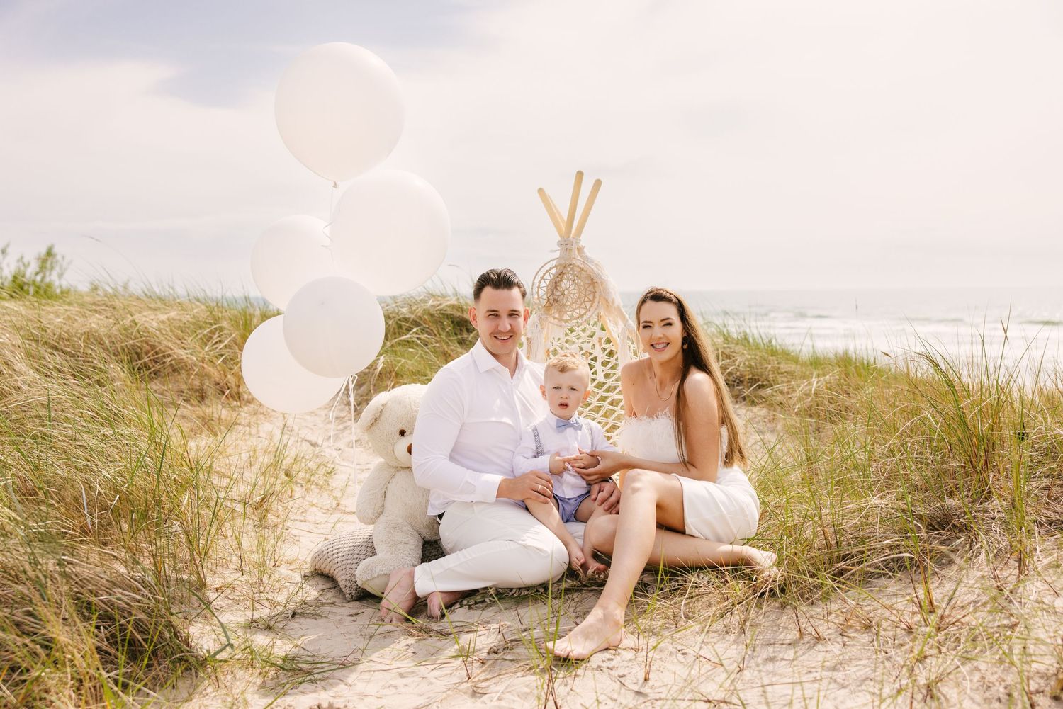 Family photo session setup on beach with white decor and natural elements.