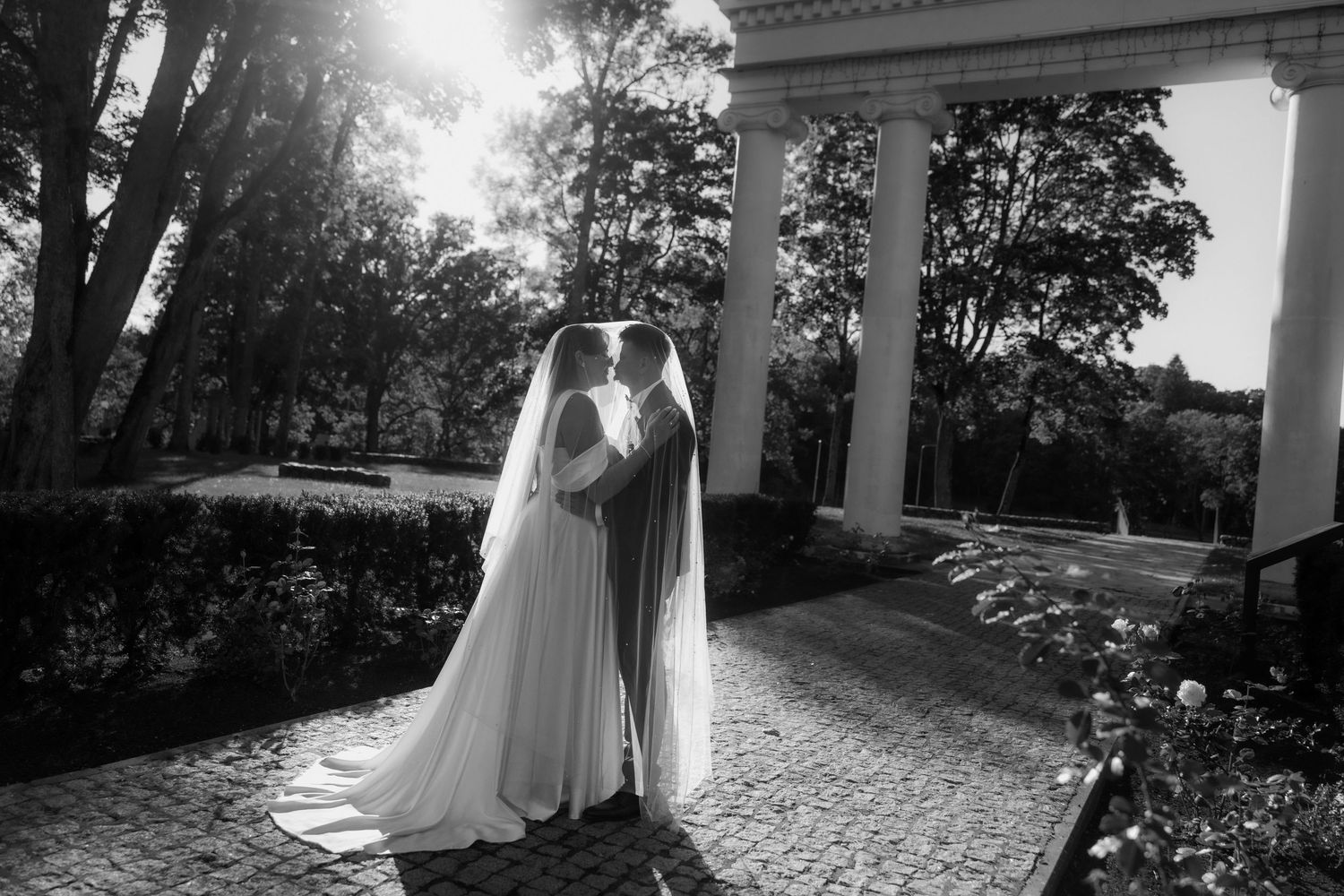 Silhouette of a wedding couple against bright sunlight near a classical columned structure.
