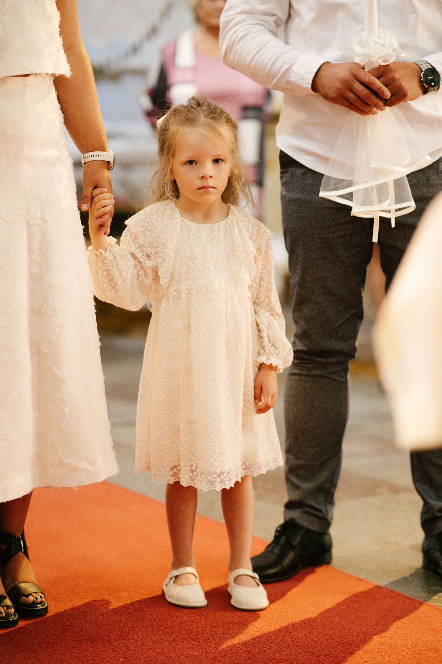 Small children in white lace dresses standing on a red carpet at a formal event.