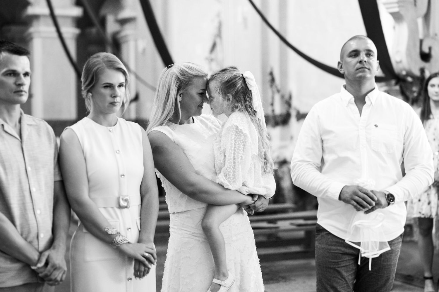 A black and white photo shows a group of people standing together at a formal event wearing light colored attire.