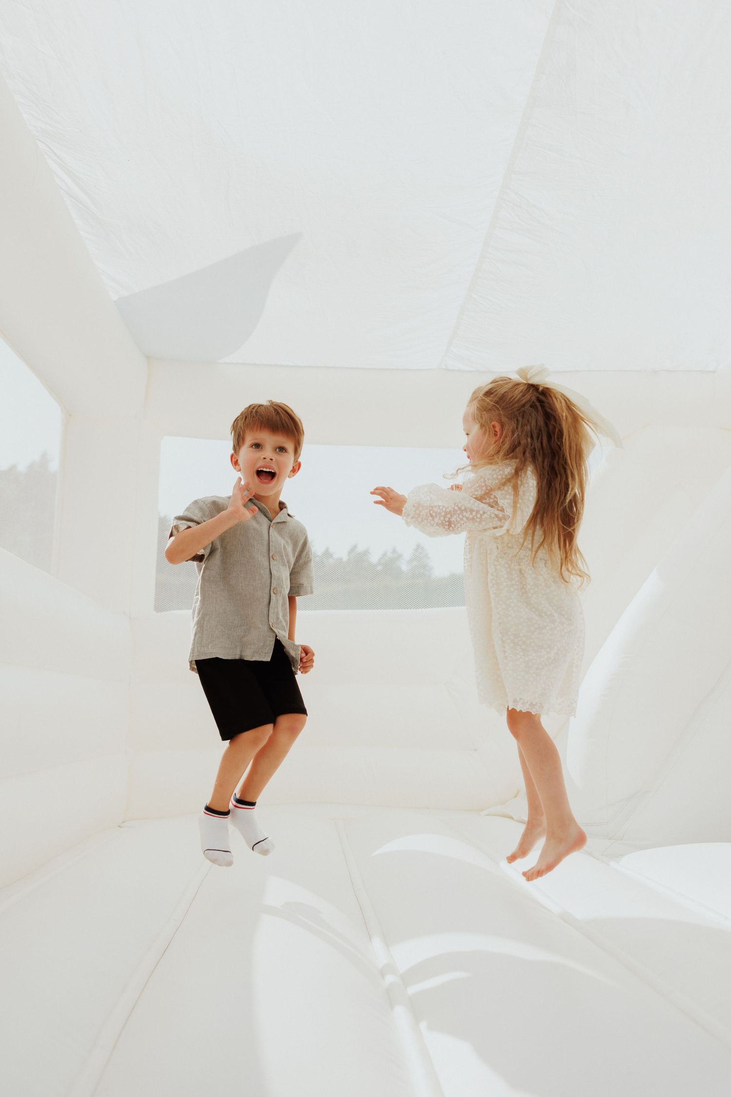 Two children in white room jumping and playing together in a minimalist setting.