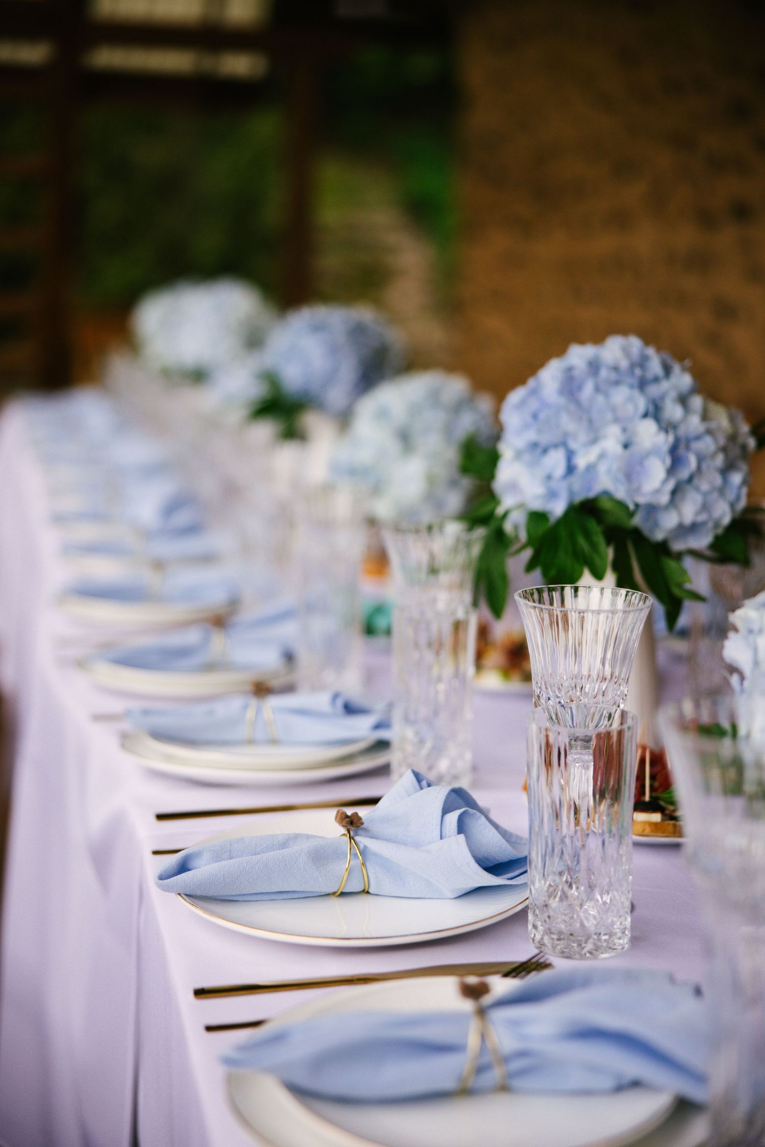Elegant wedding table setting with blue hydrangeas, crystal glasses, and white linens.