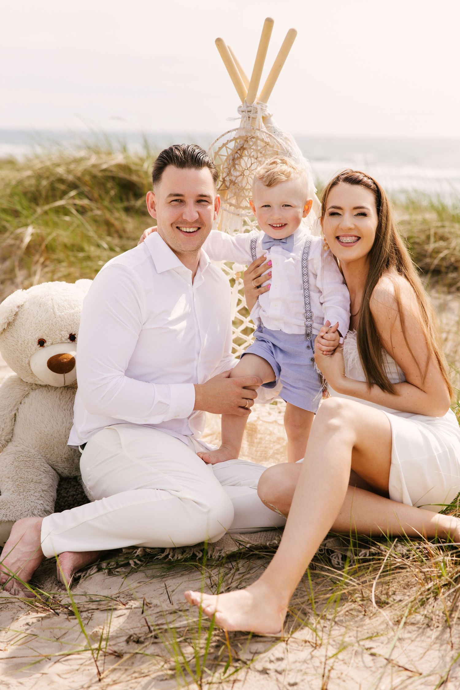 Family portrait session on a sandy beach with coordinated white and blue outfits.