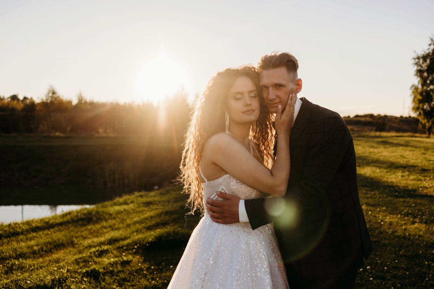 Romantic couple embraces during golden hour sunset photoshoot in a scenic outdoor meadow with lens flare.