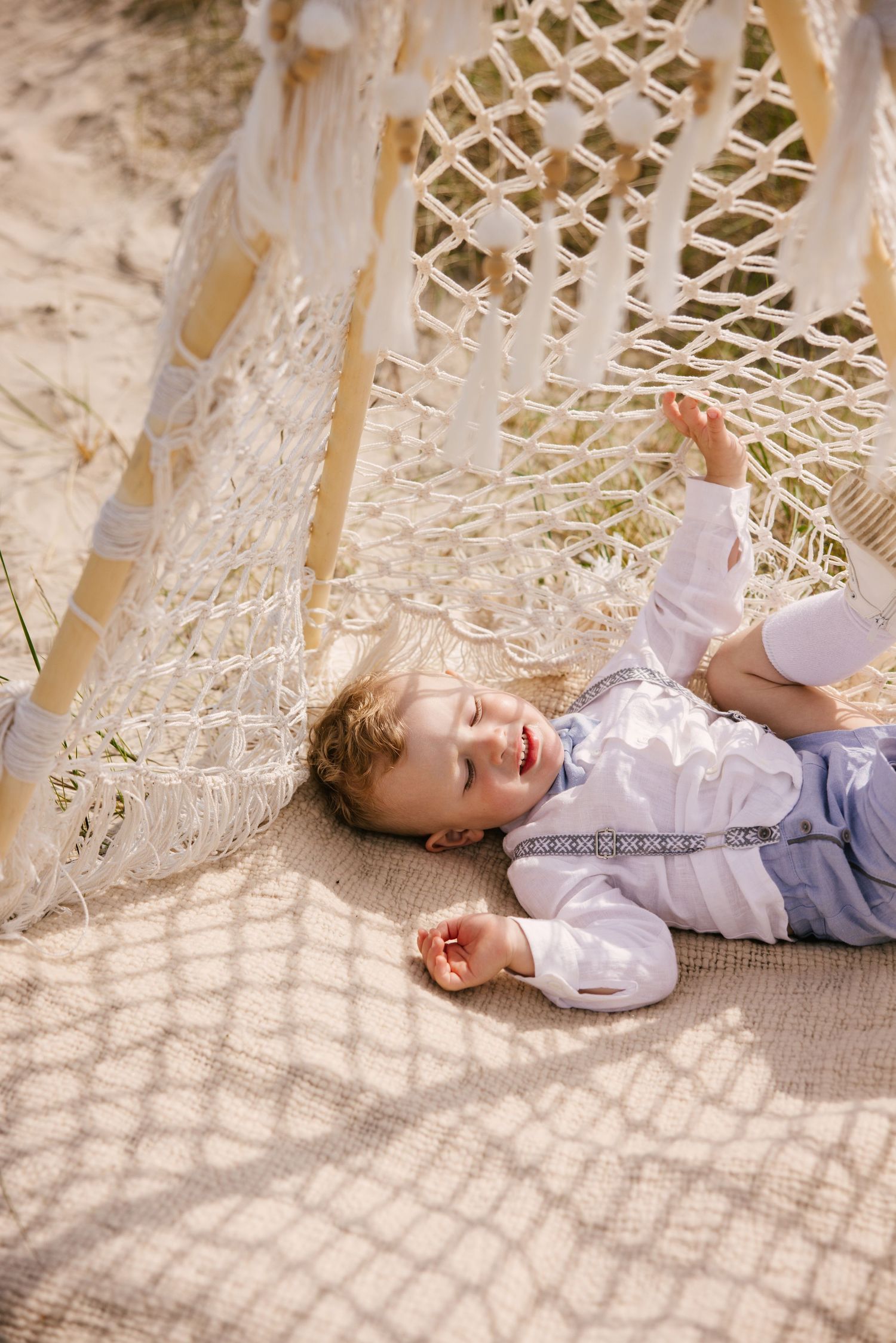 Child relaxing under decorative lattice canopy on sandy beach.
