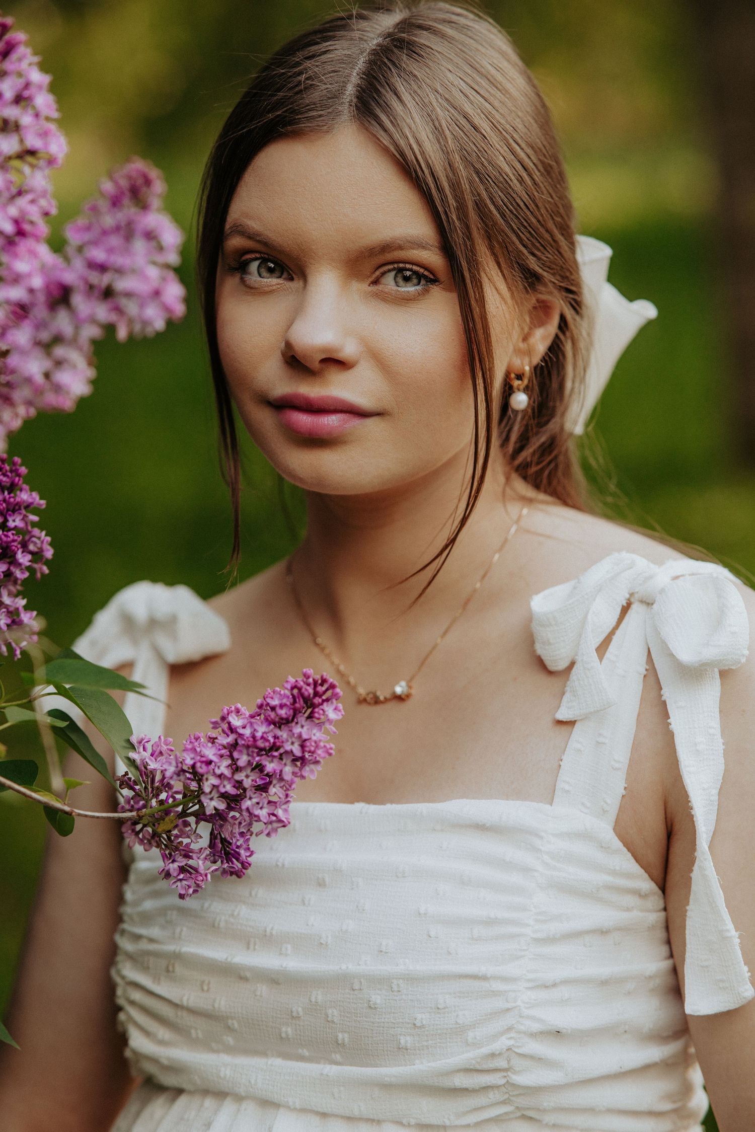 White dress with bow details photographed near blooming lilac flowers in springtime.