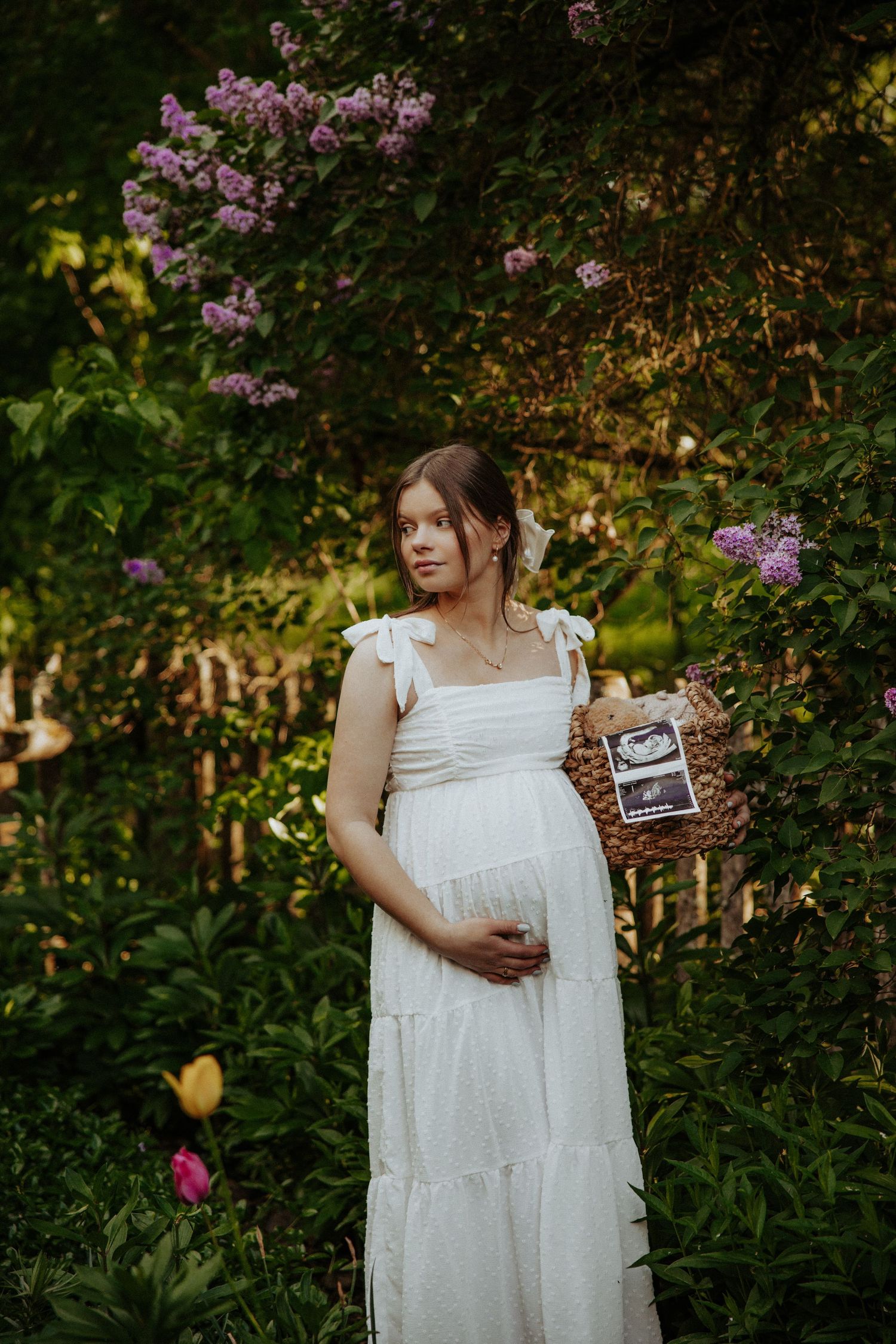 White dress against blooming lilac bushes with a vintage photograph held in hand.