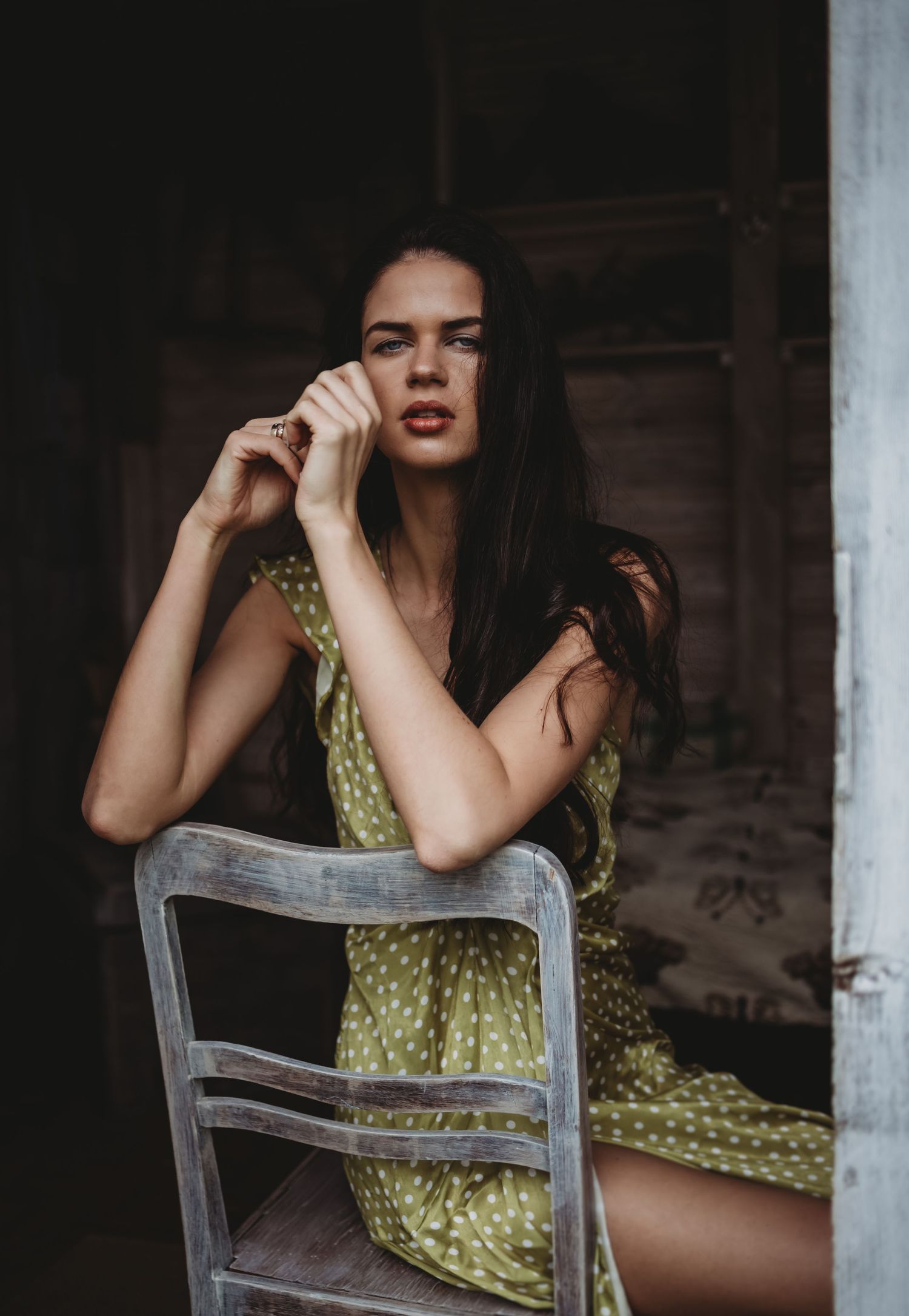 Dramatic indoor portrait with vintage chair in moody lighting.