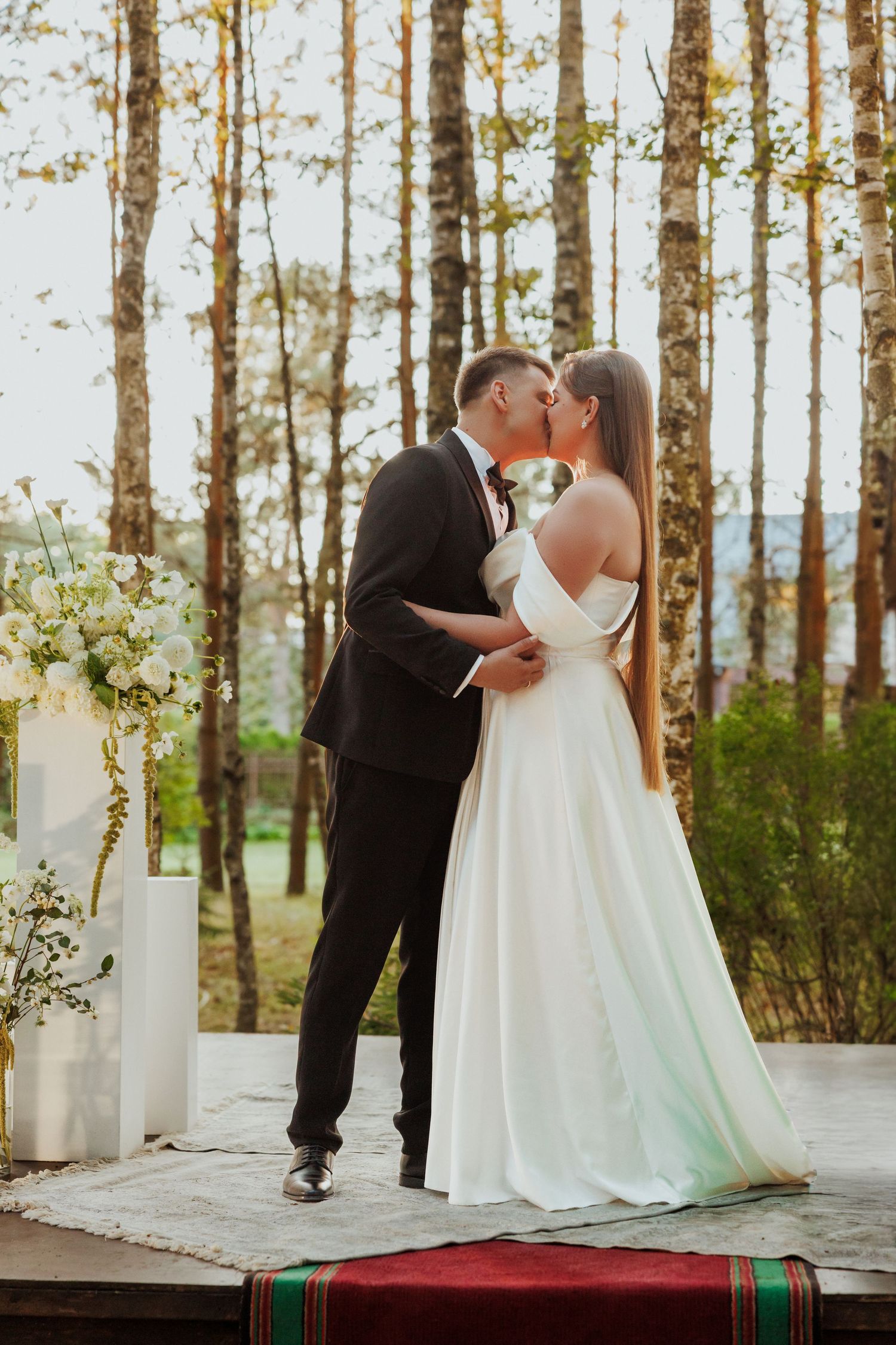 Wedding ceremony on a raised platform surrounded by birch trees in natural outdoor setting.