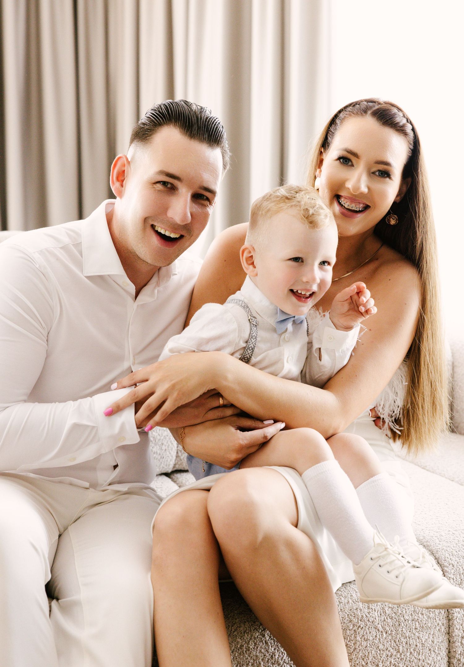 Family in white outfits sharing joyful moment on couch together.