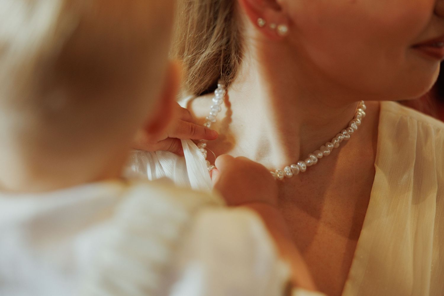 A close-up view of a person wearing delicate pearl drop earrings and a white dress in warm lighting.