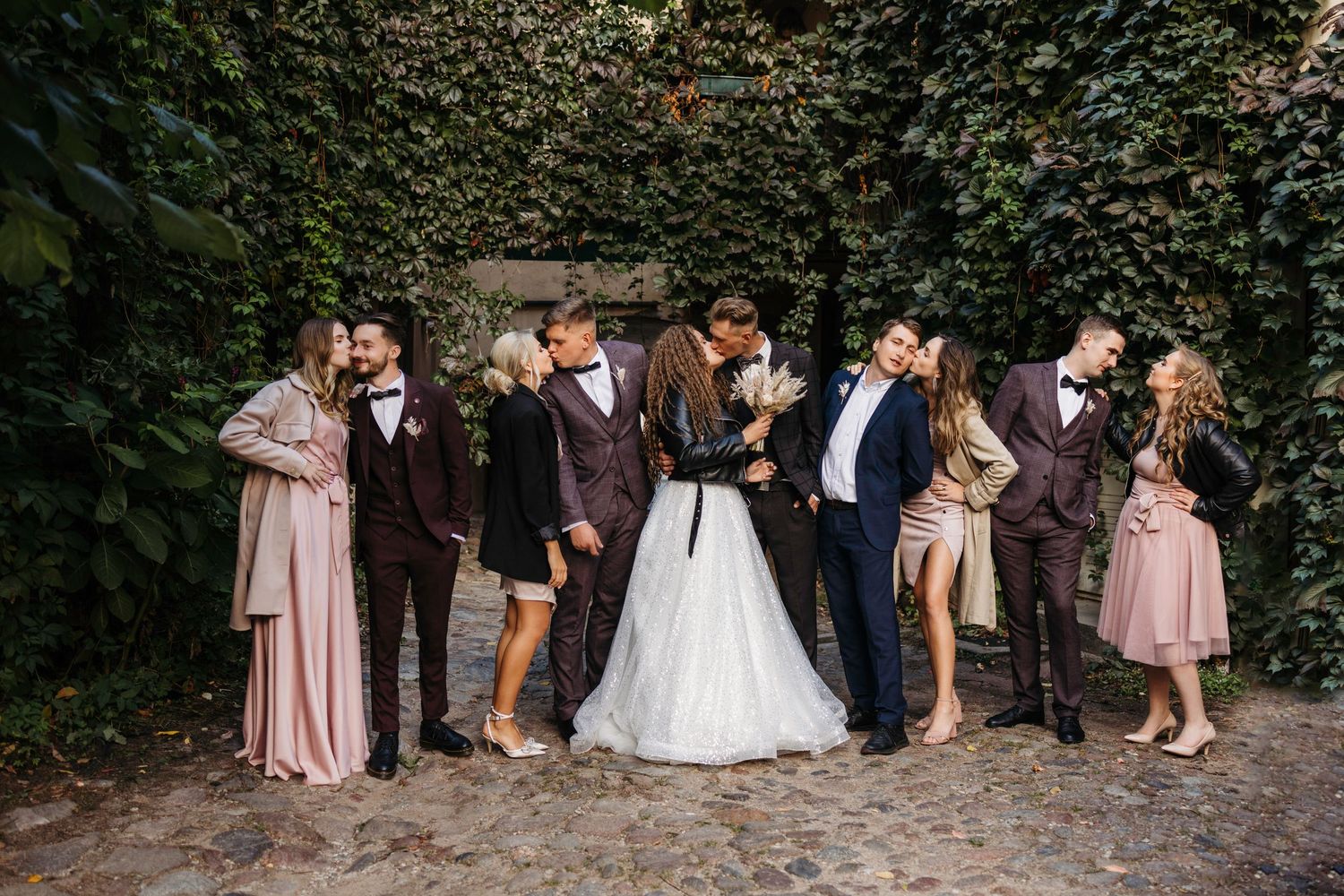 Wedding party gathered for group photos against a lush ivy-covered wall backdrop.