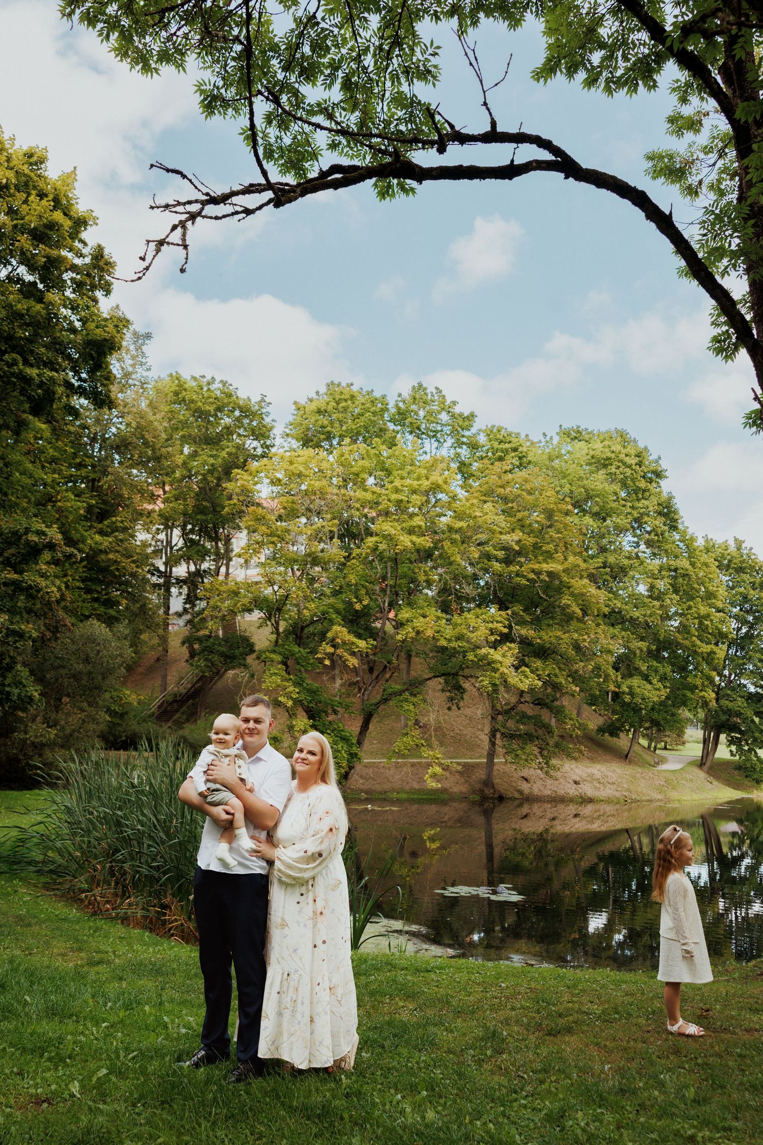 Family portrait by a pond with overhanging tree branch and natural scenery.