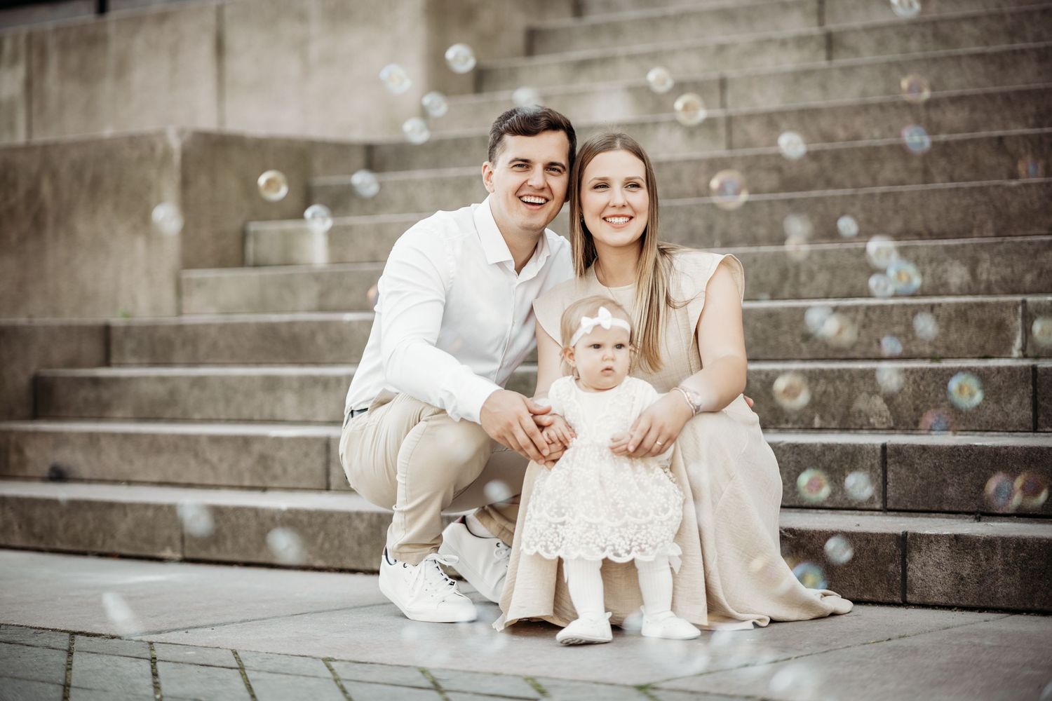 A series of black and white photos showing a family sitting together on stone steps in coordinated neutral outfits.