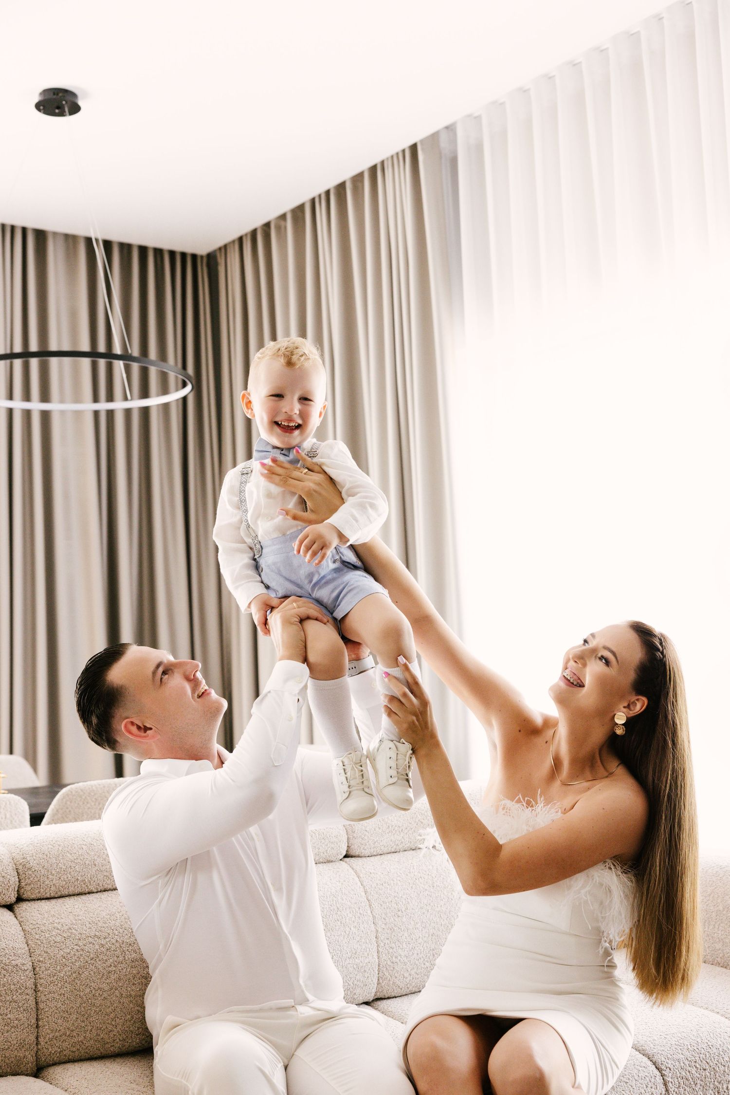 A joyful family moment in a modern living room as parents lift and play with their laughing toddler.