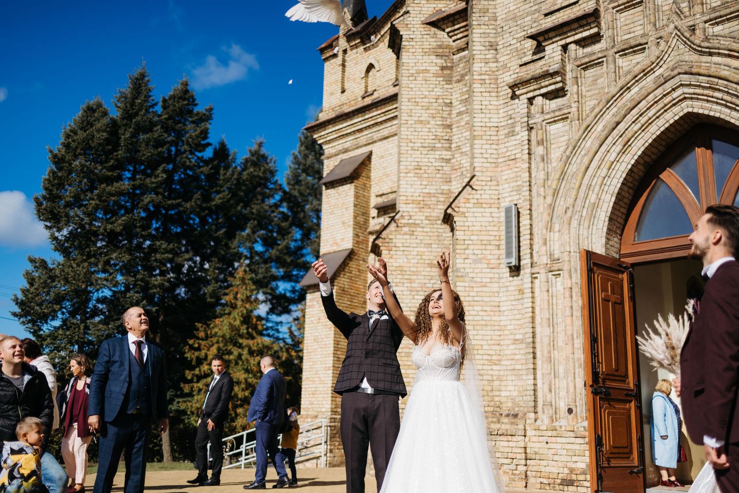 Stone church facade with arched entrance serves as backdrop for outdoor wedding festivities.