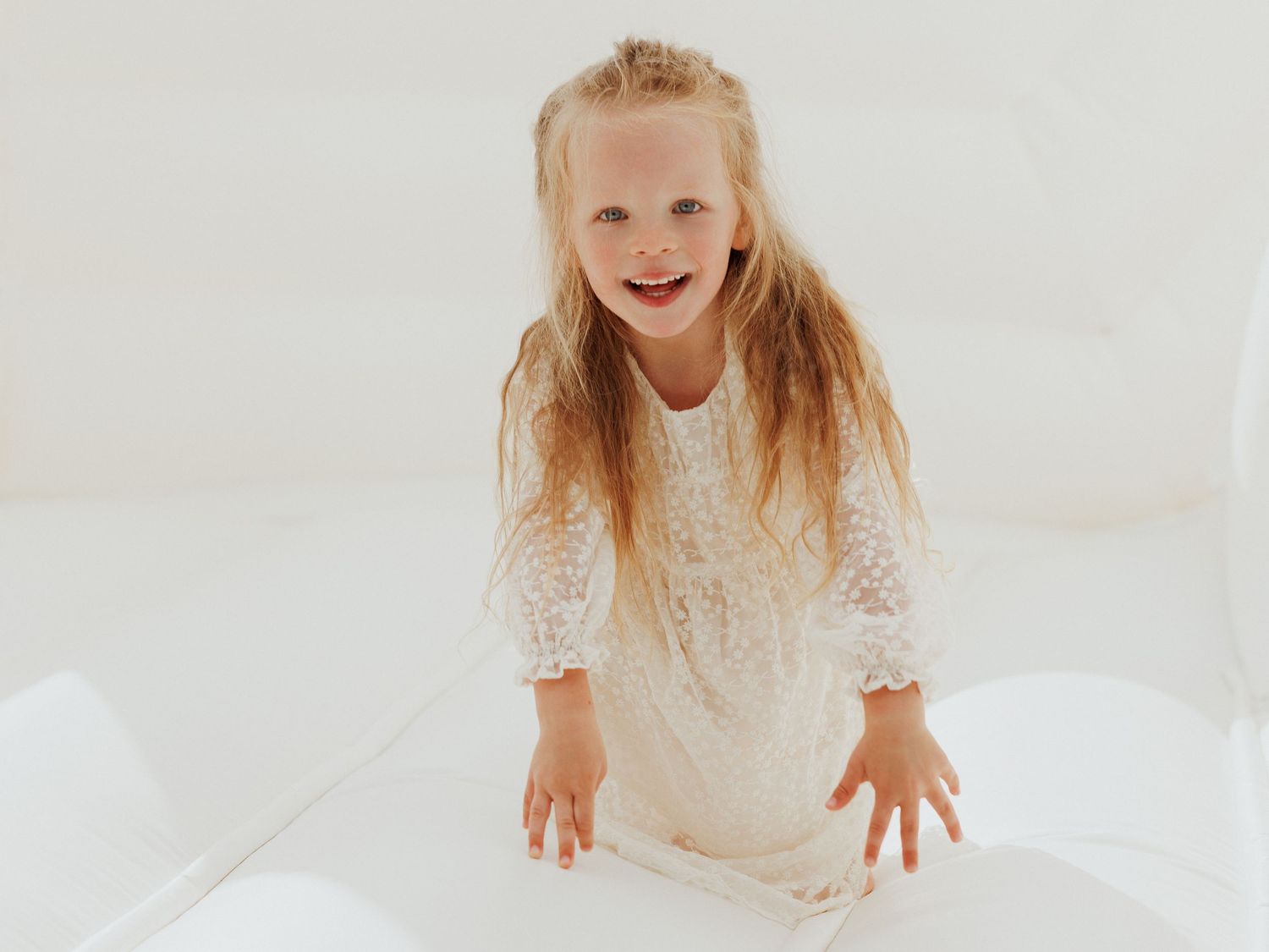A child in a white lace dress plays and poses on a bright white background.