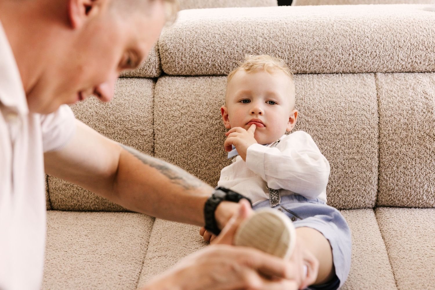 A baby and adult play together on a beige couch, showing a sweet moment of interaction and bonding.